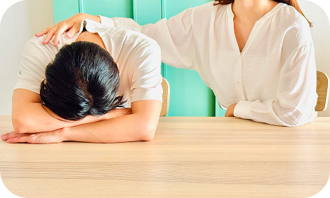 テーブルに頭を伏せてうつむく人の肩に、そっと手を置いて寄り添う人